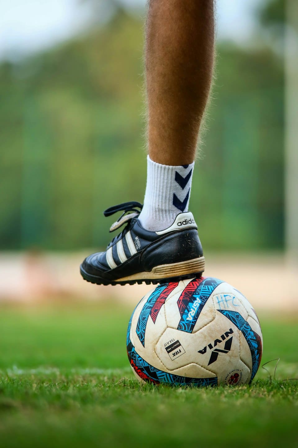 Football boot resting on a soccer ball on green grass.
