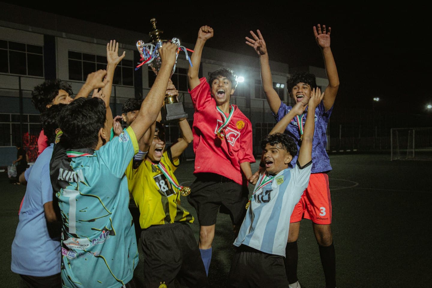 Men celebrating with a trophy on a football field at night.