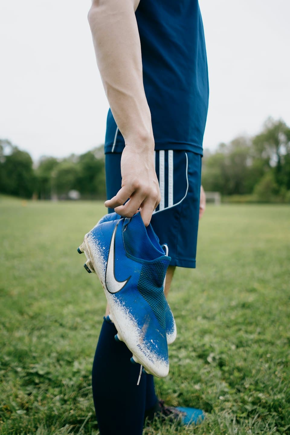 Soccer player holds a dirty boot on a grass field.