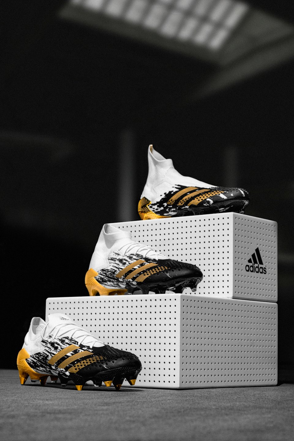 Three football boots displayed on white risers on a dark floor.