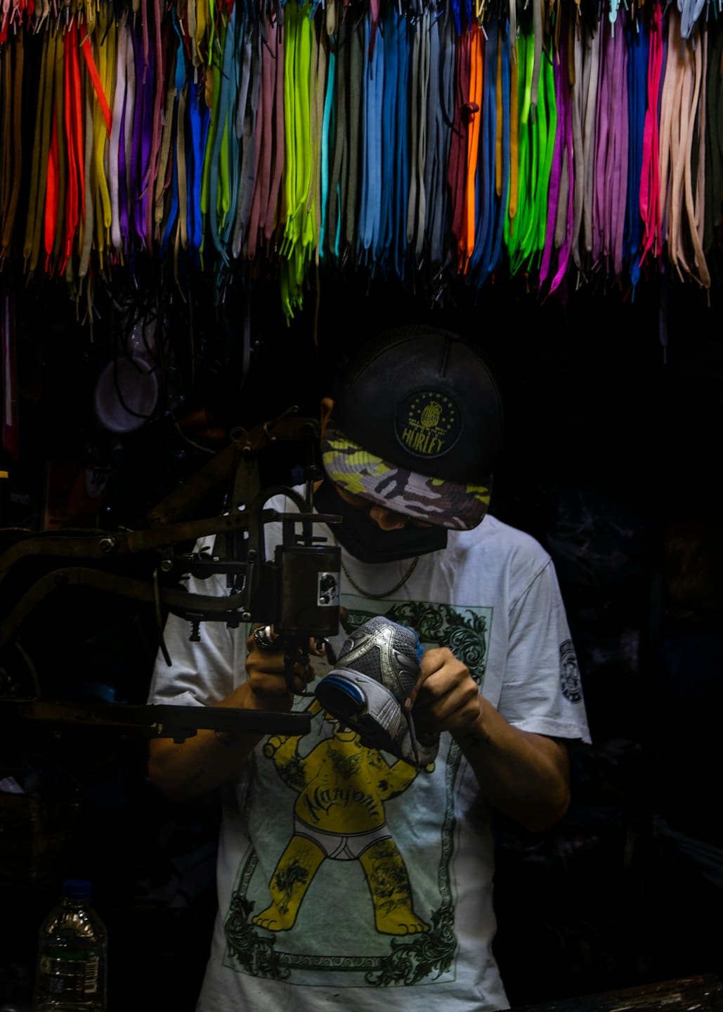 Man in mask sewing a sneaker in workshop.